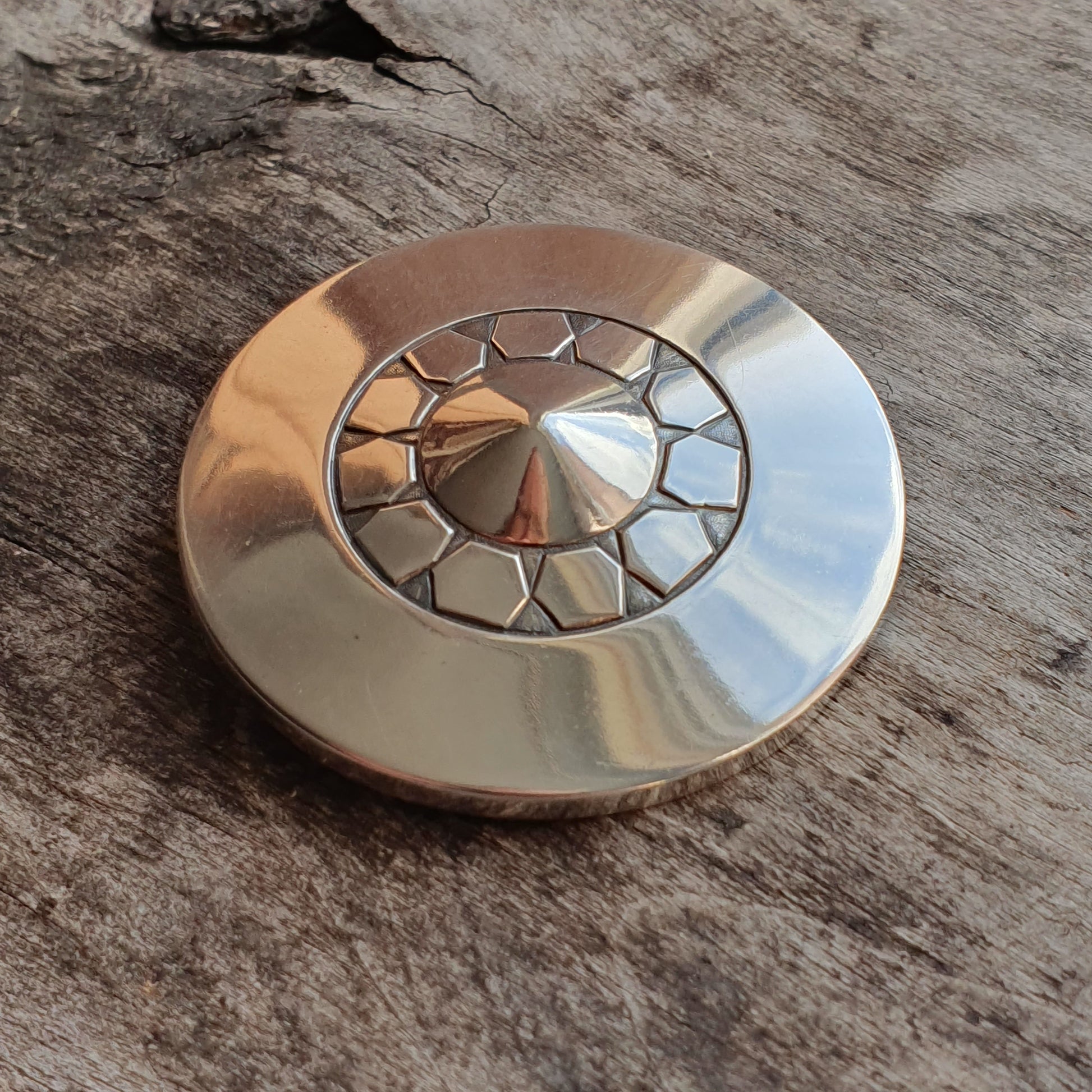 Metallic fidget spinner with a geometric pattern on a wooden surface.