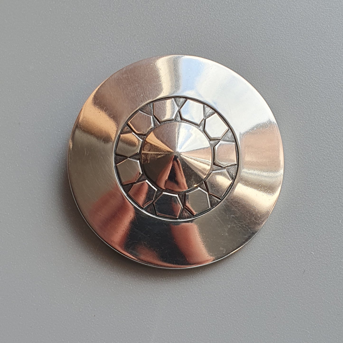 Metallic circular brooch or pin with a decorative clock face design.