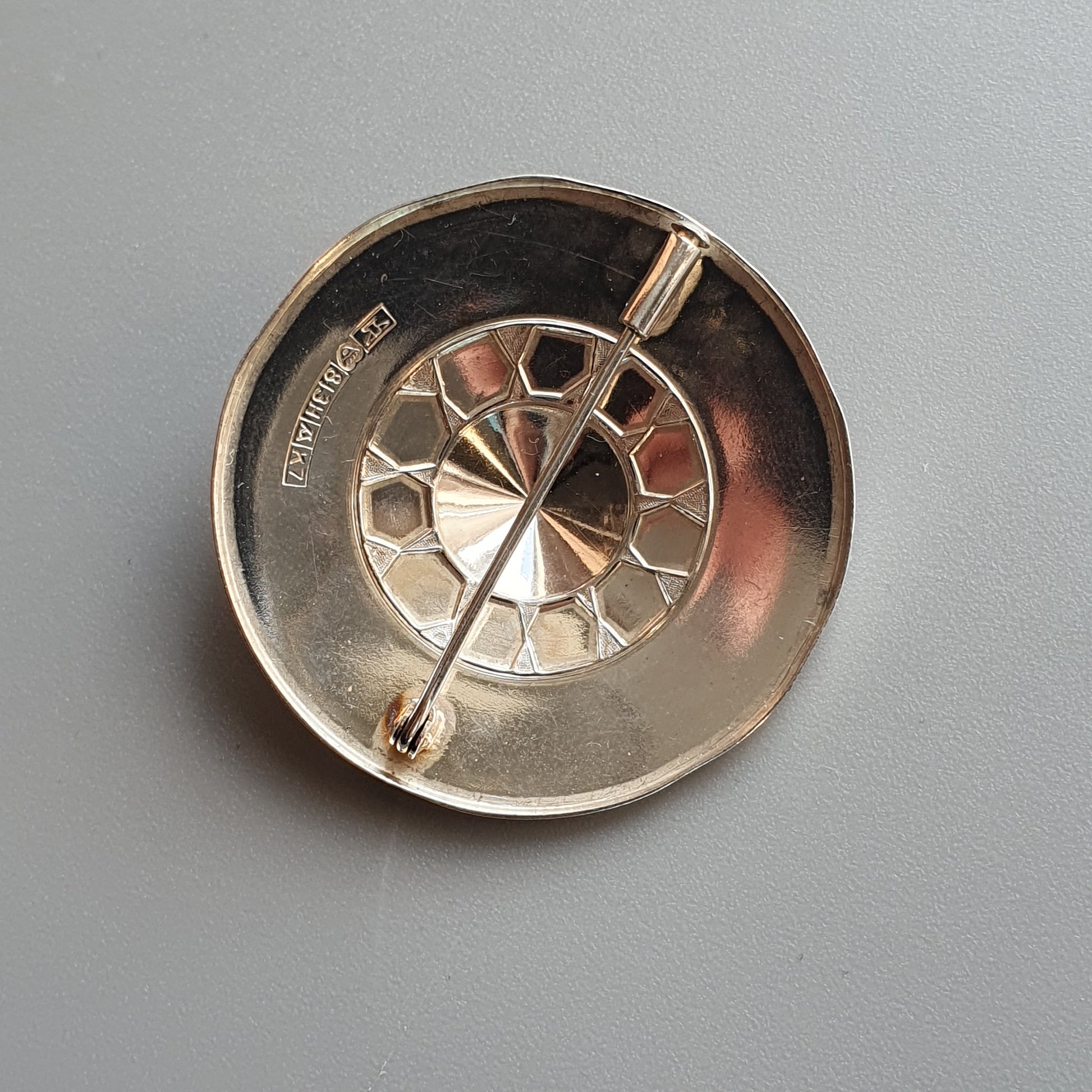 Circular metal brooch or pin with a geometric pattern and central spoke.