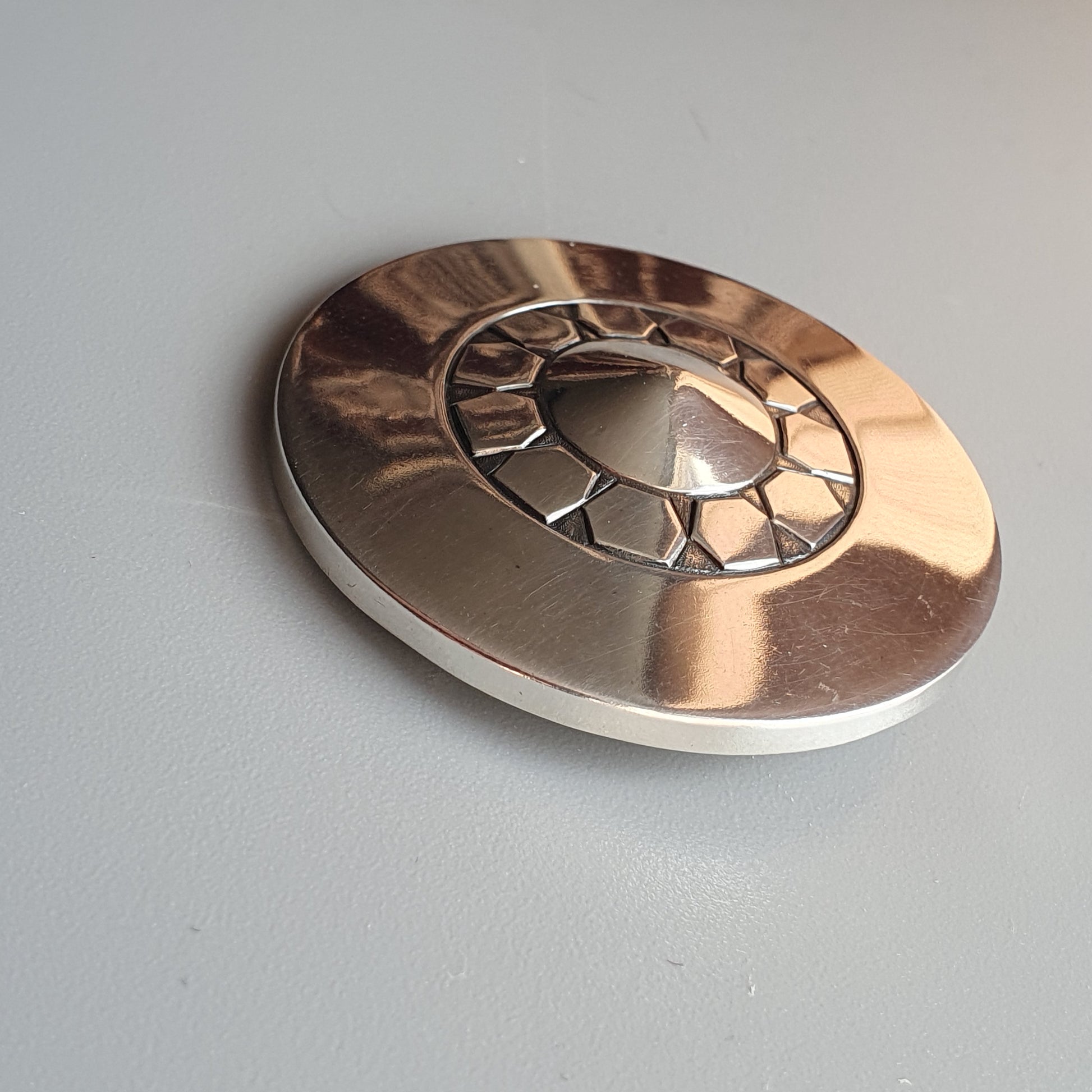 Metallic disc with a decorative circular pattern on its surface.