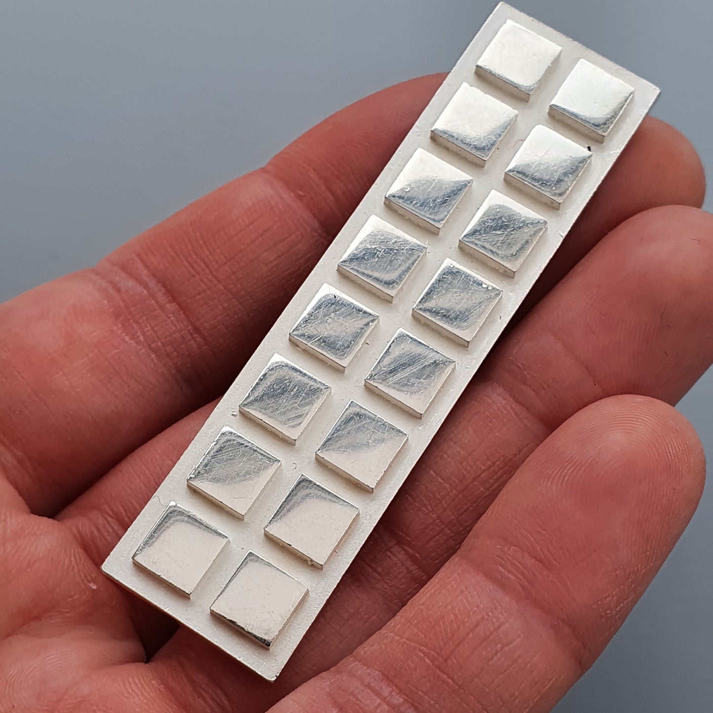 Blister pack of square-shaped pills next to Finnish Minimalist Rectangular Silver Brooch