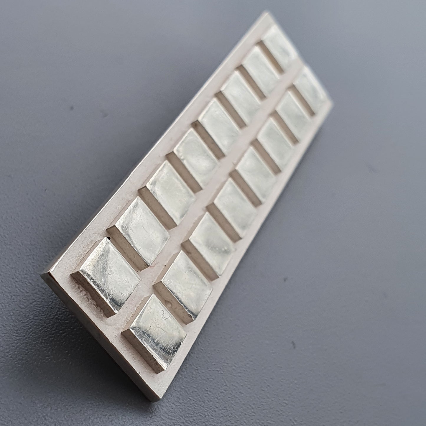 White plastic ice cube tray with minimalist rectangular compartments for silver brooch display