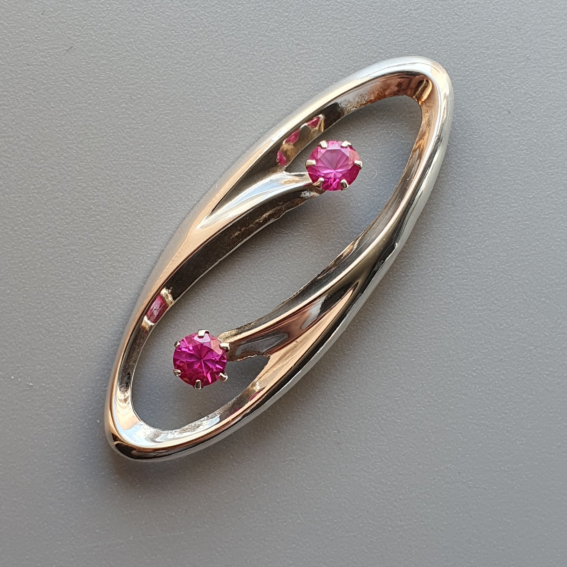 Elegant oval-shaped gold brooch featuring two pink gemstones.