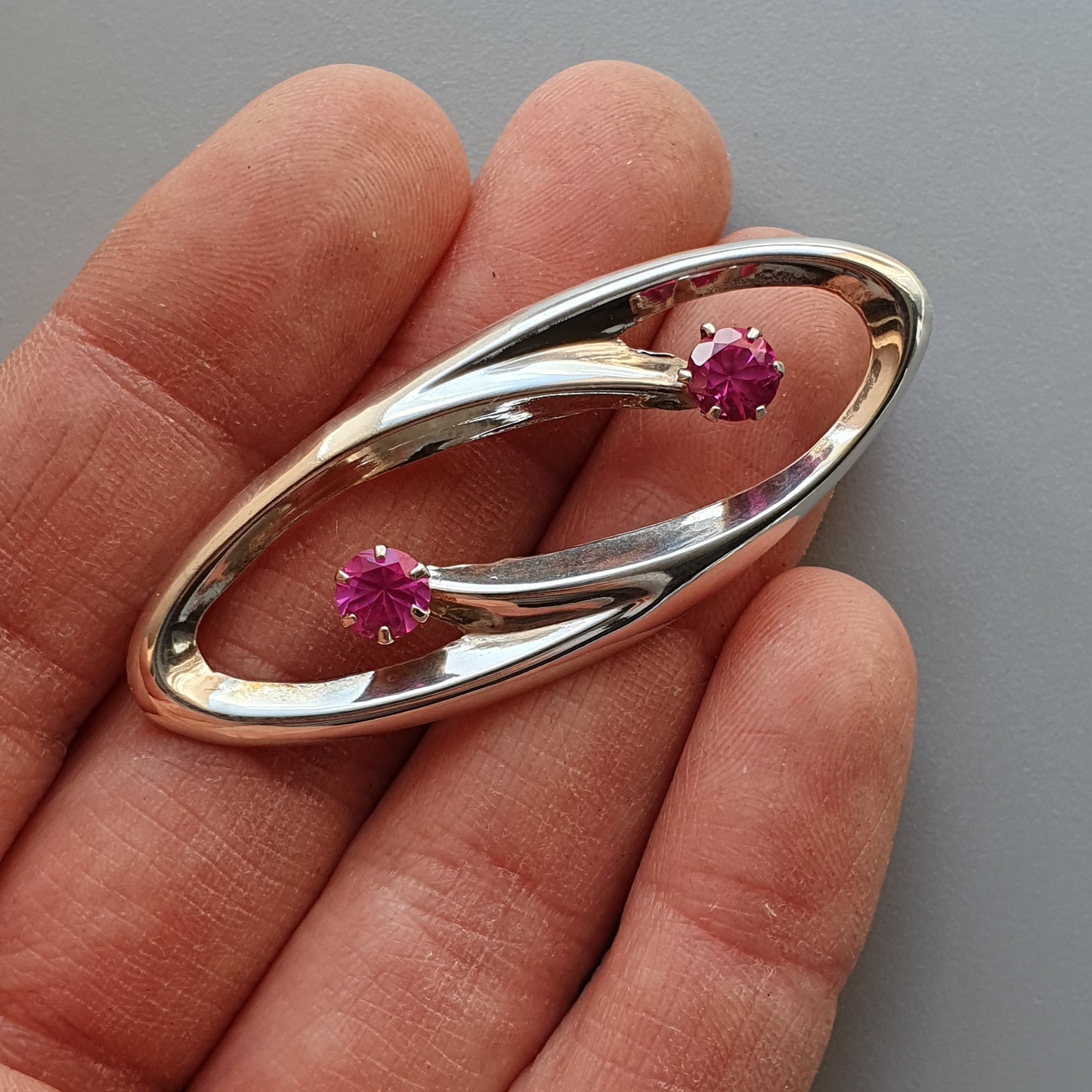 Oval-shaped silver brooch with two pink gemstones.