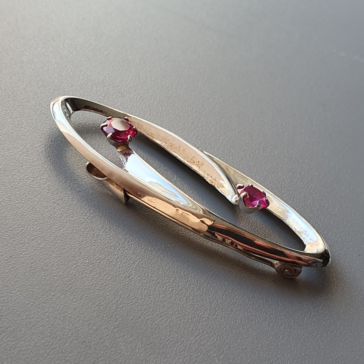 Elegant gold brooch with two small pink gemstones set in an elongated oval design.