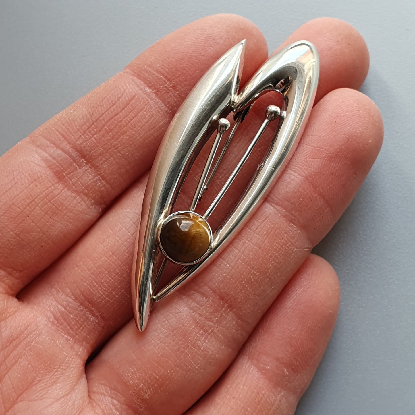 Silver leaf-shaped brooch with a golden bead accent.