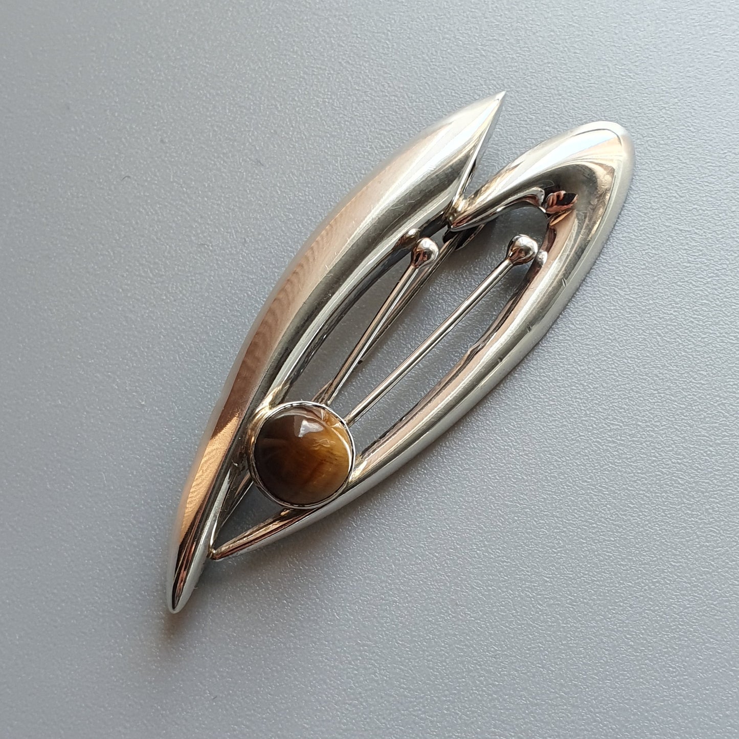 Silver brooch with an abstract leaf-like shape and a brown gemstone accent.