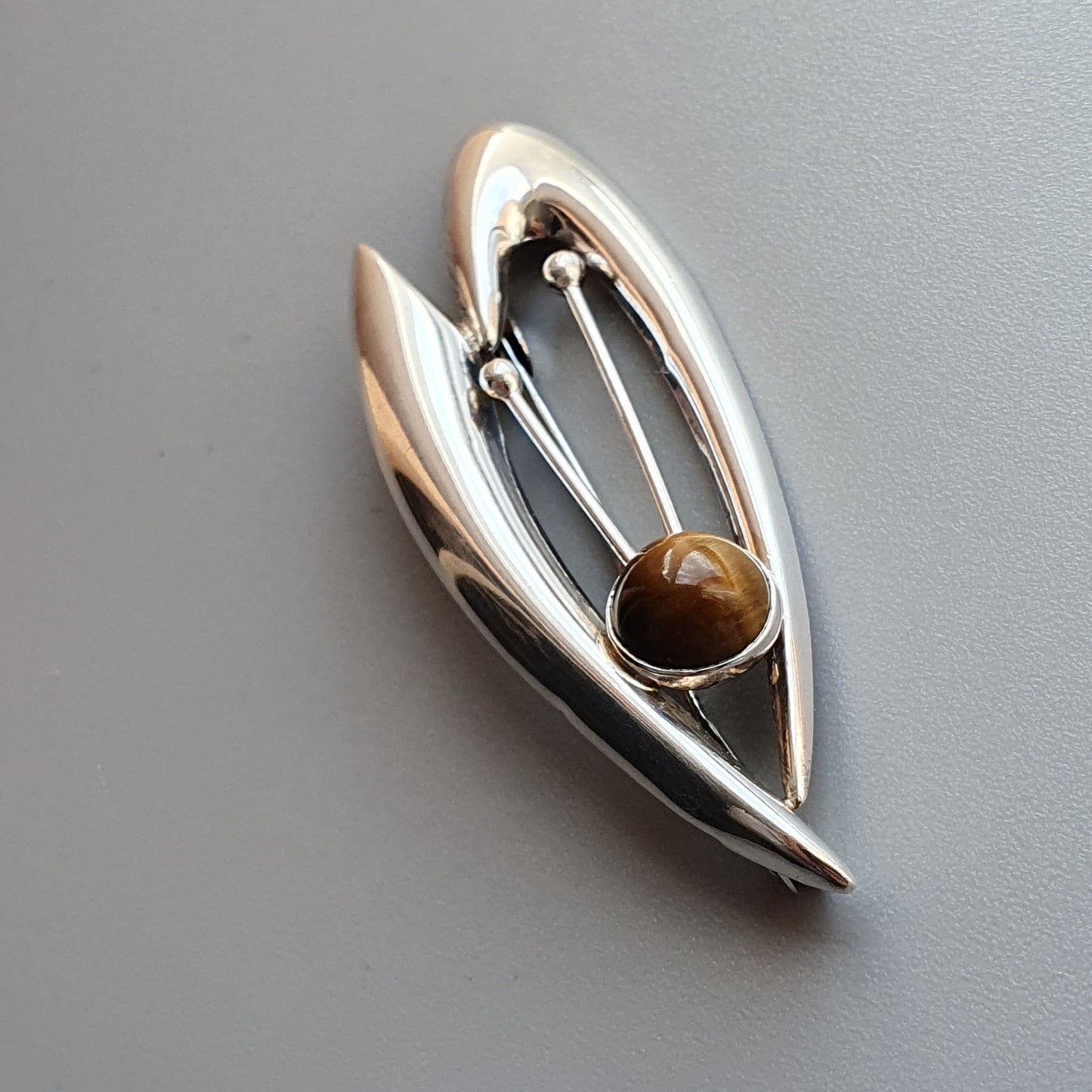 Modernist silver brooch with an abstract leaf-like shape and a brown gemstone accent.