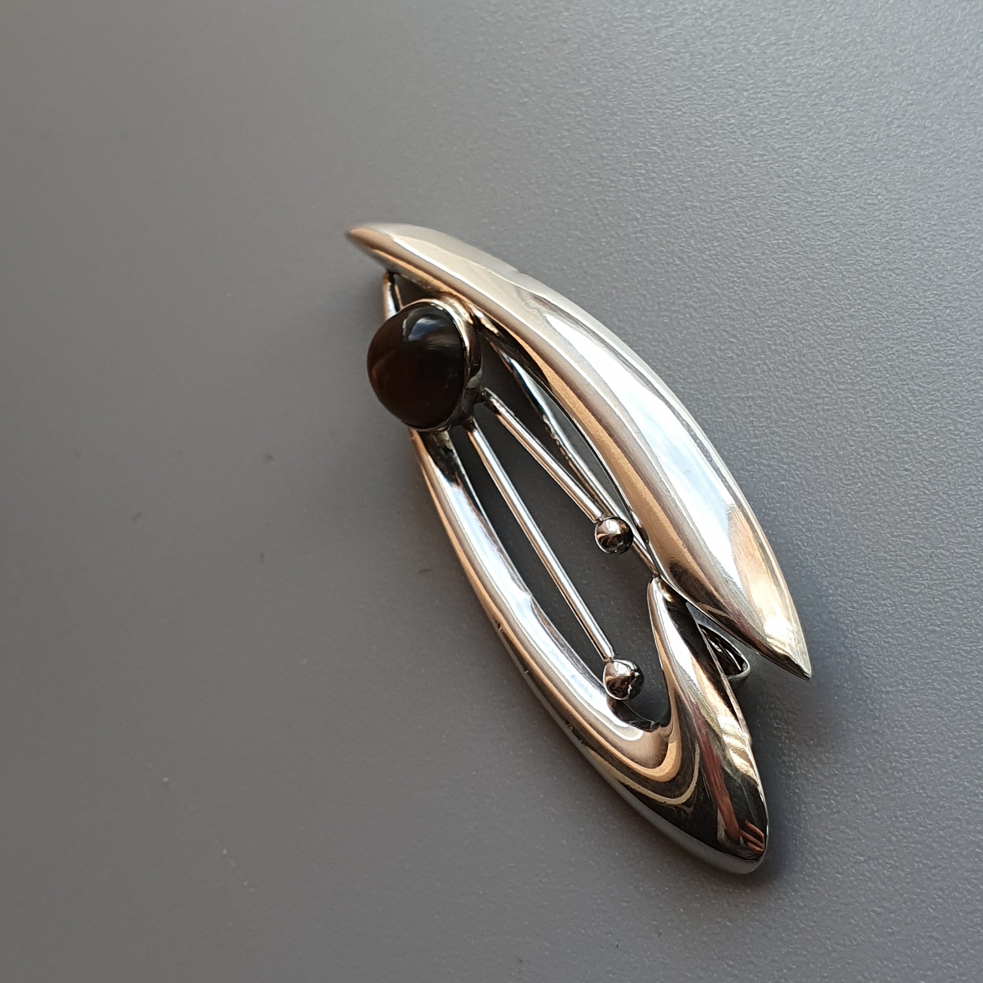 Sleek silver brooch with an oval shape and a dark gemstone accent.