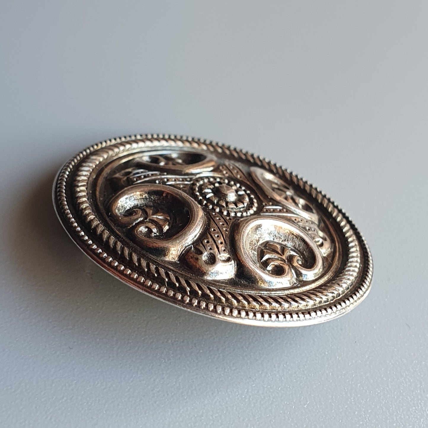 Ornate silver brooch with intricate swirling patterns and beaded details.