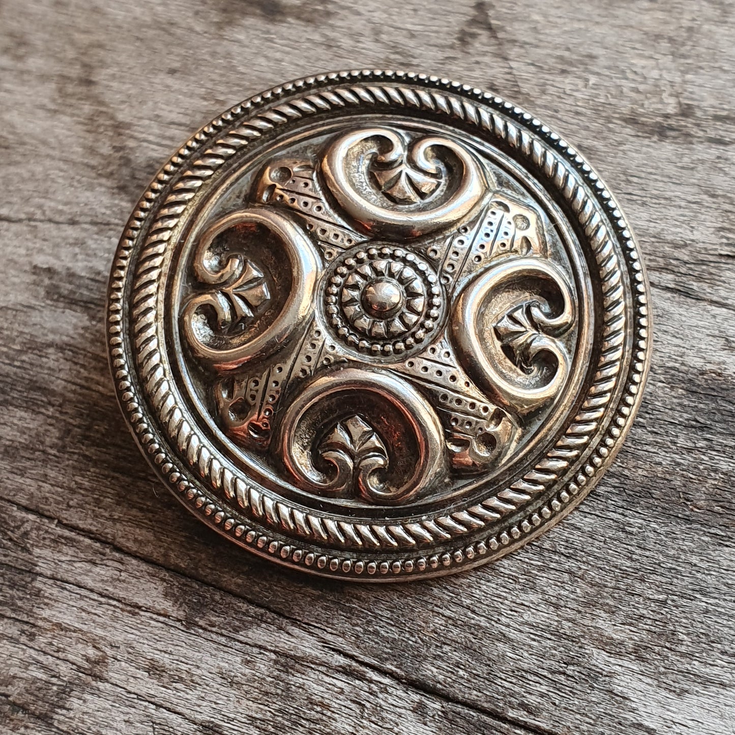 Ornate silver brooch with intricate Celtic-inspired swirl patterns and a circular design.