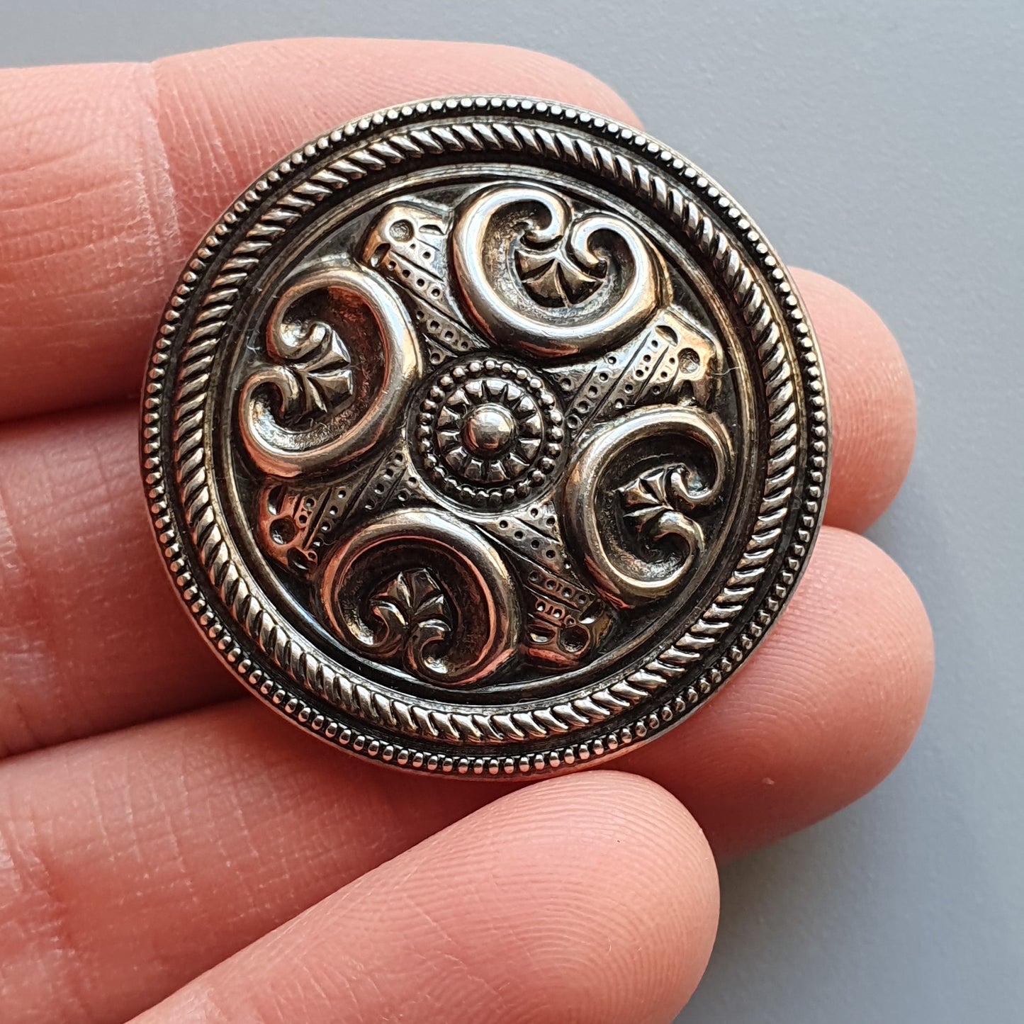 Ornate metal button with intricate swirling patterns and a circular design.