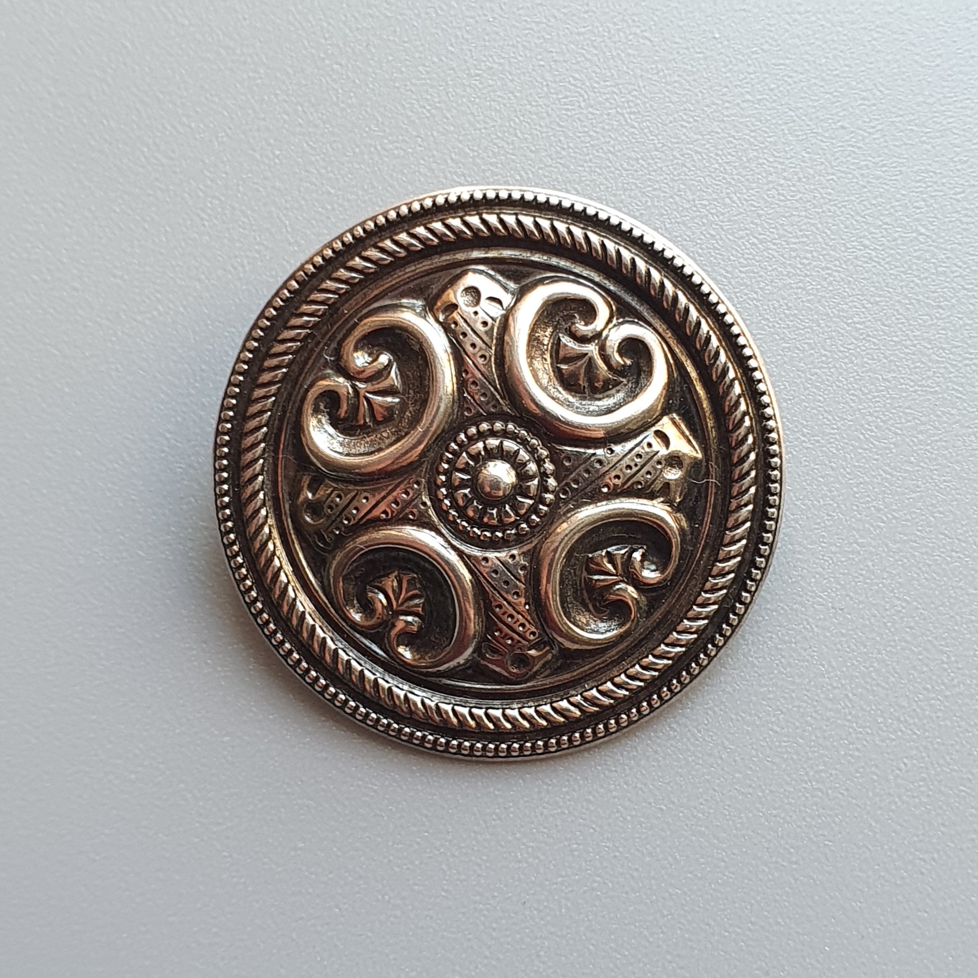 Ornate circular silver brooch with intricate swirling patterns and floral motifs.