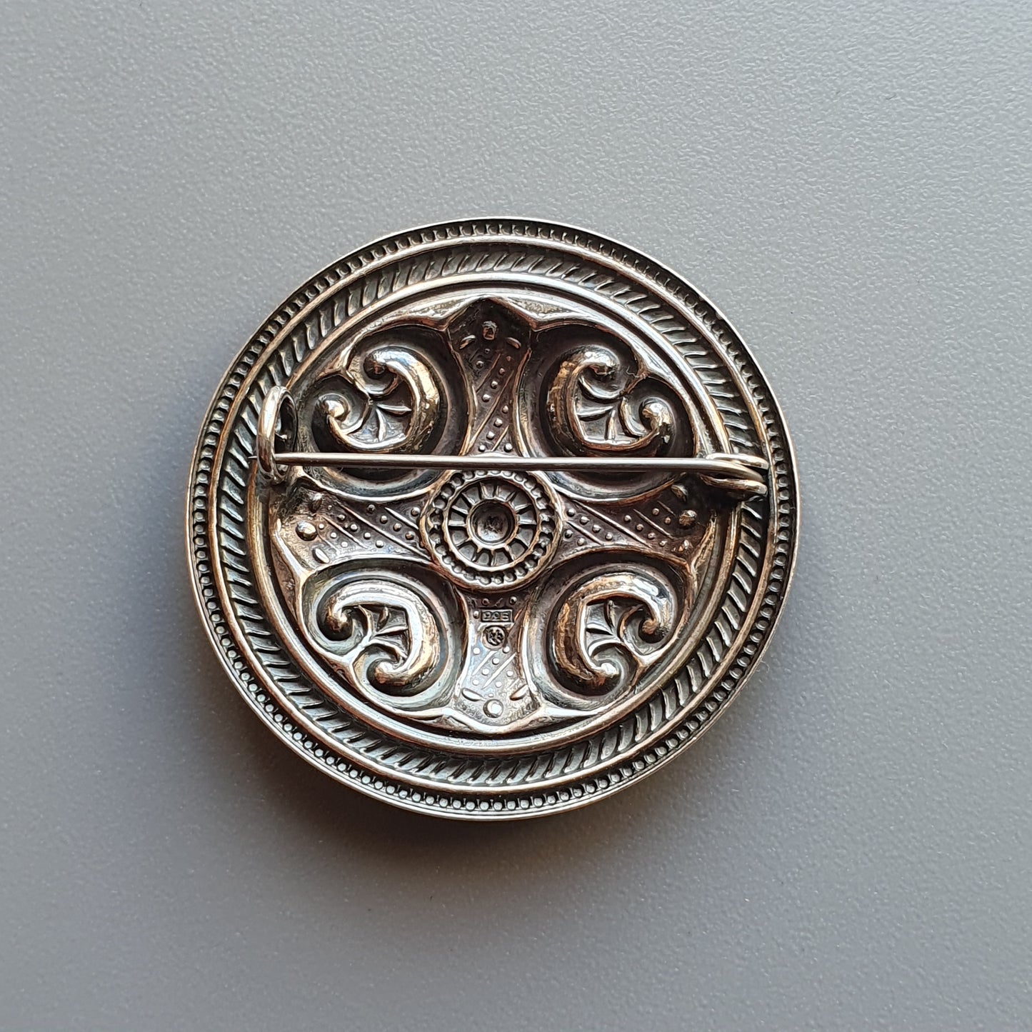 Ornate silver brooch or medallion with intricate Celtic-inspired swirling designs.