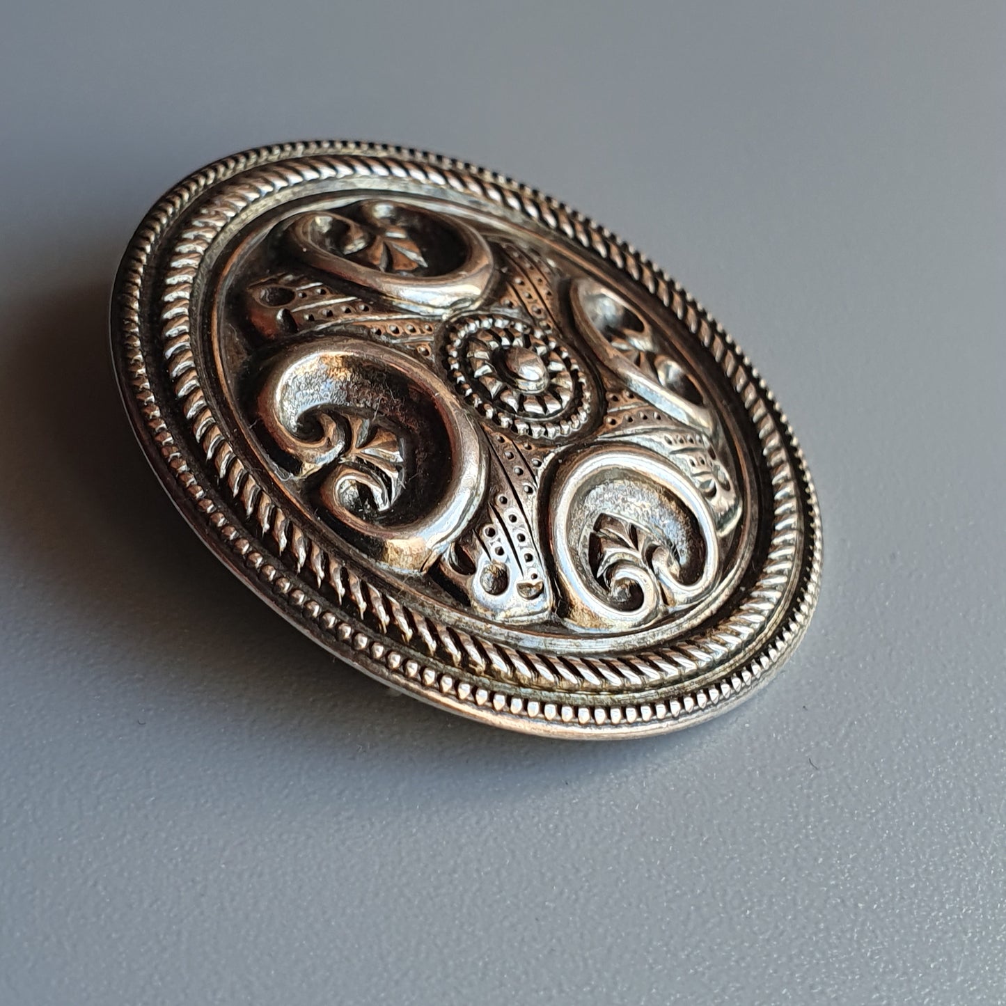 Ornate silver brooch with intricate swirling patterns and floral motifs.