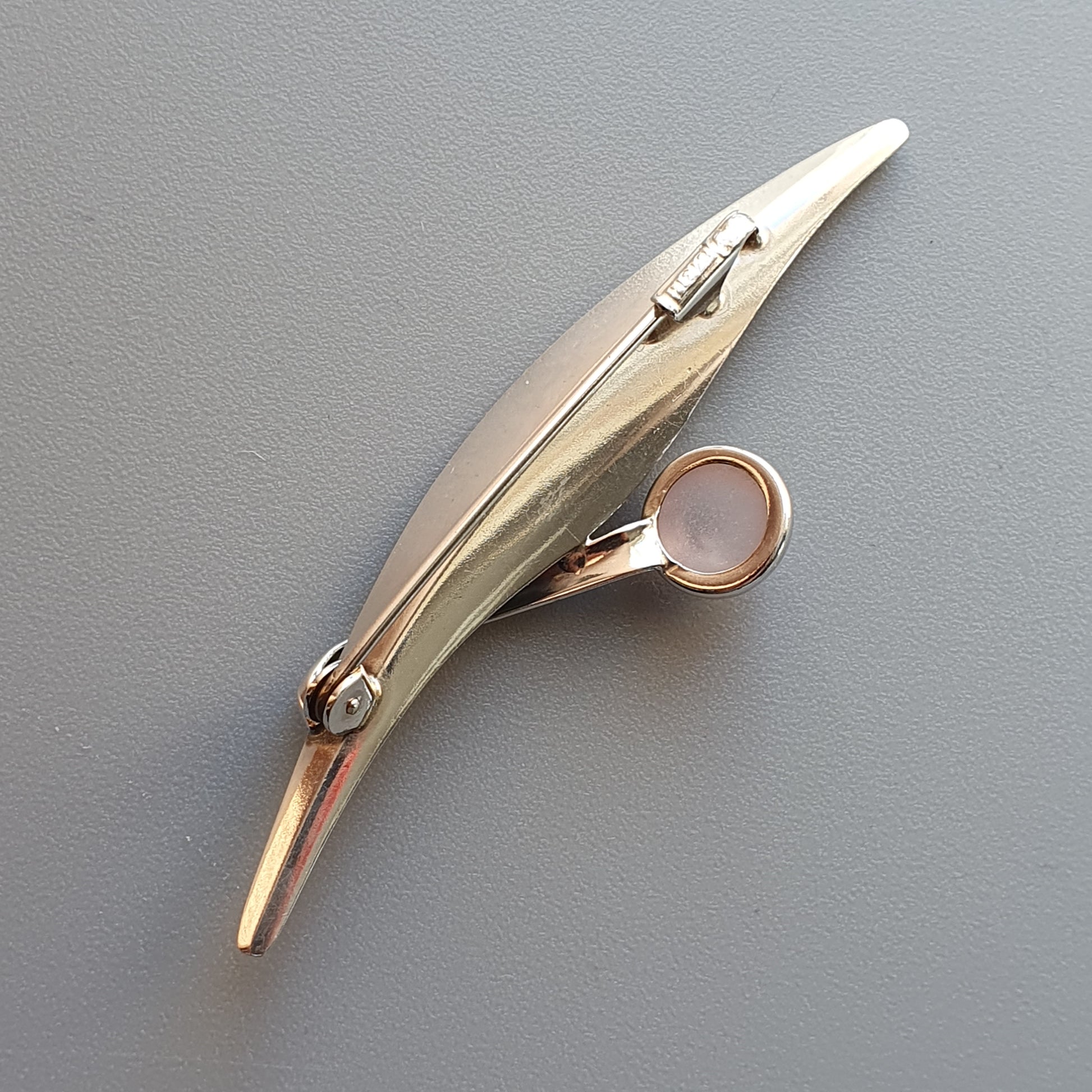 Gold-colored brooch or pin shaped like a stylized bird or dolphin.