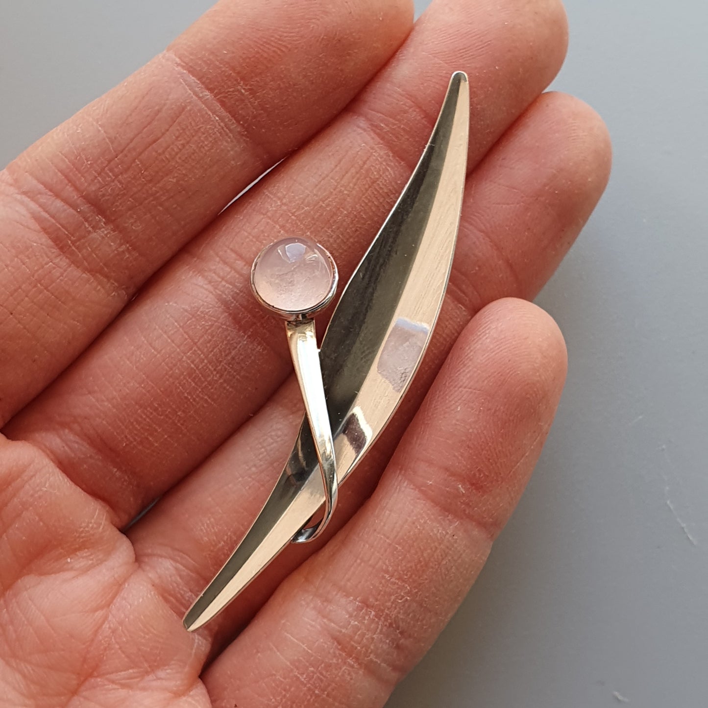 Sleek silver brooch or pin with a curved shape and small round gemstone accent.