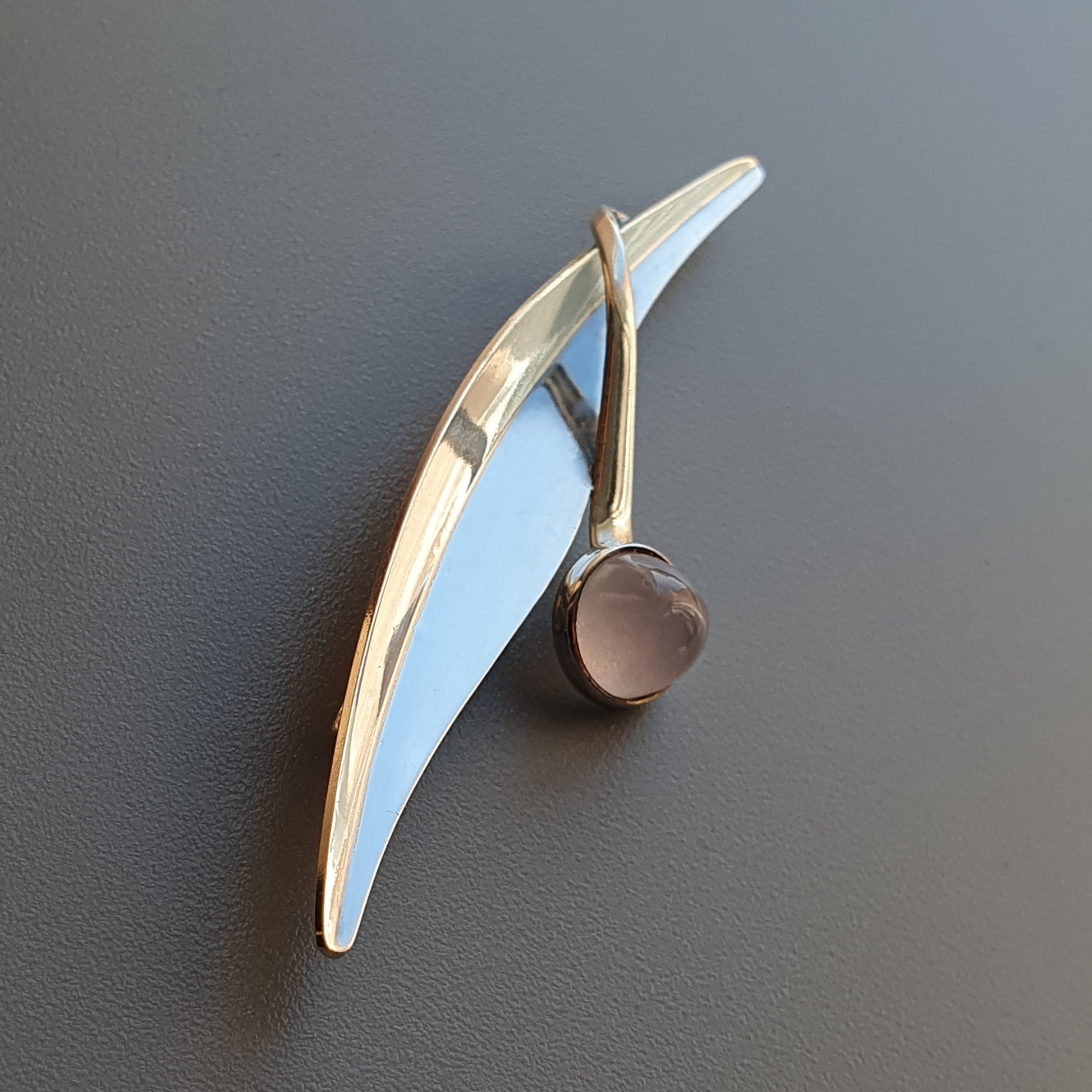 Sleek, curved brooch or pin with a light blue enamel accent and metallic elements.