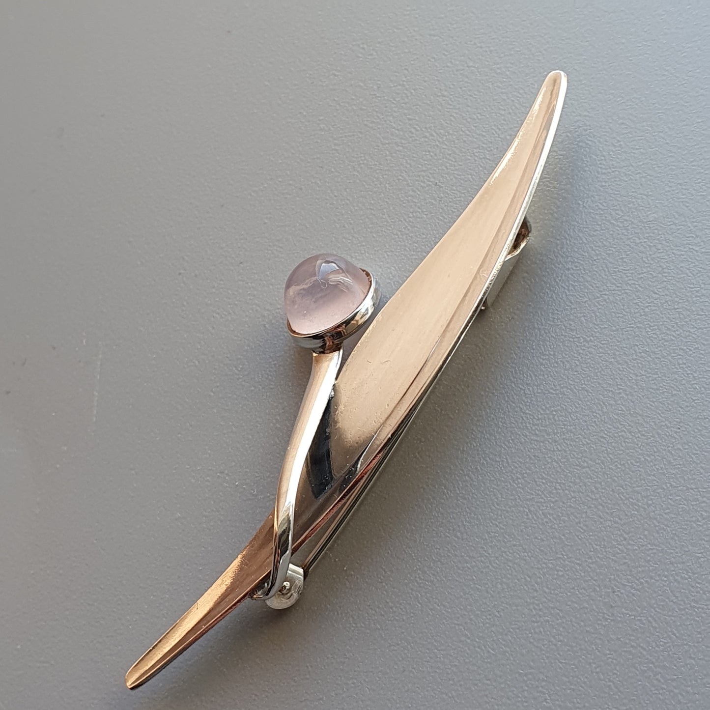 Elegant gold-toned tie clip with a small pink gemstone or crystal accent.