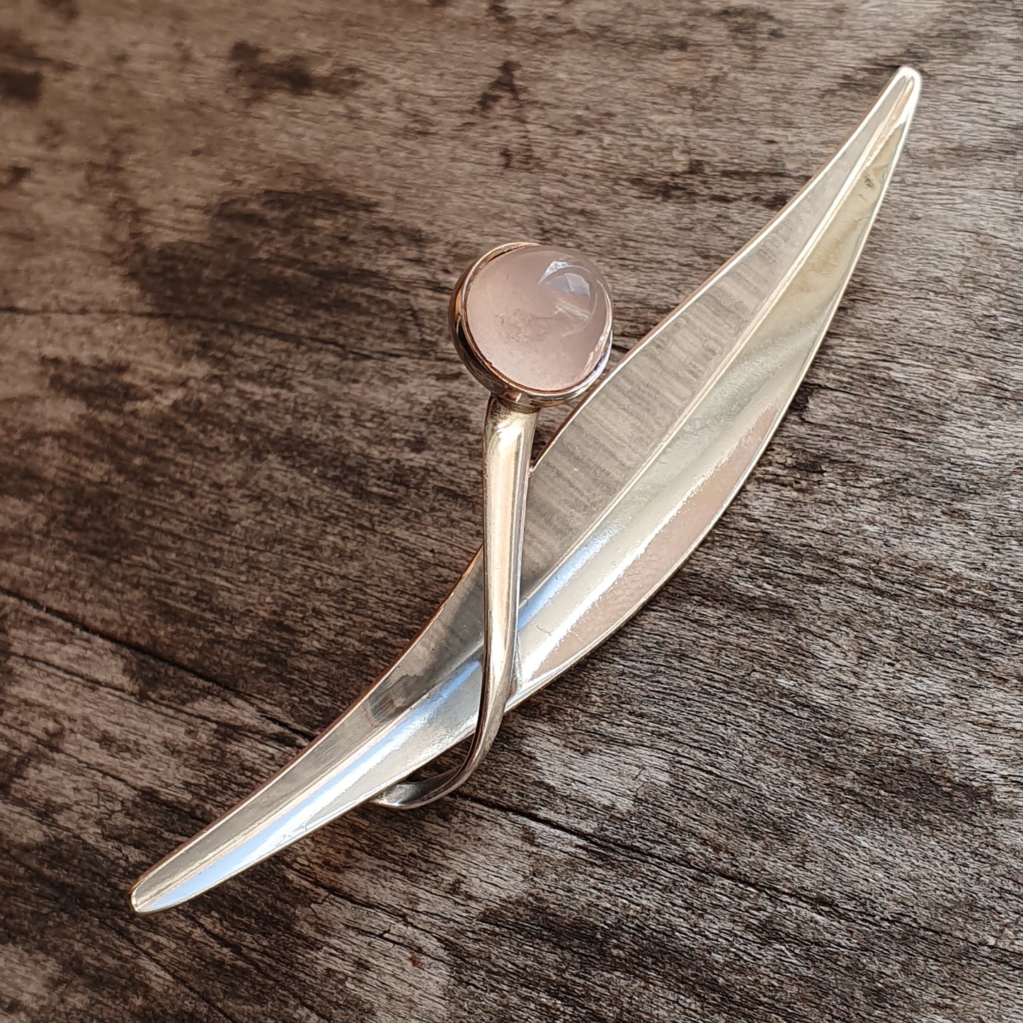 Silver brooch or pin shaped like a stylized leaf or feather with a pale pink gemstone.