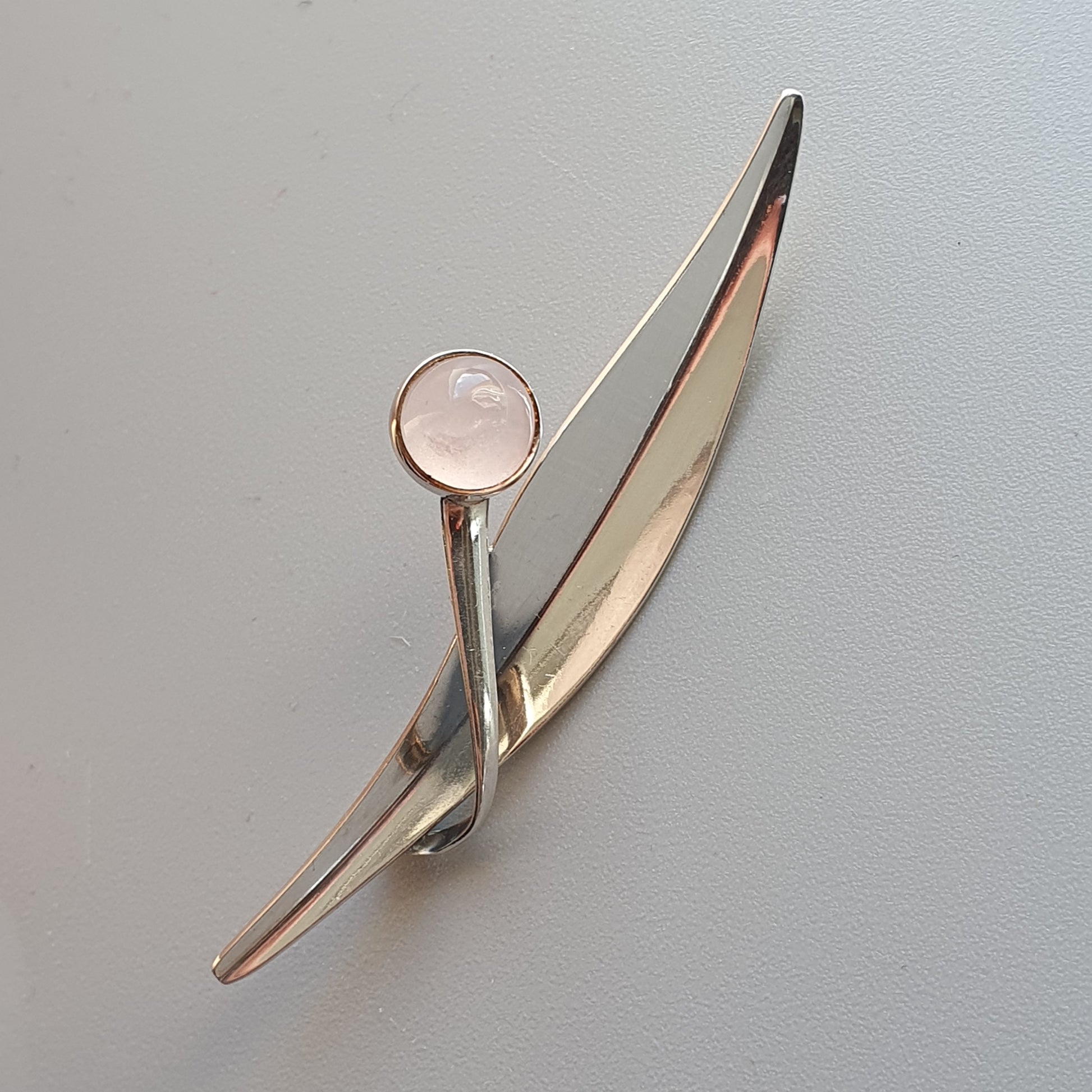 Sleek silver brooch with a curved design and a round pink gemstone.