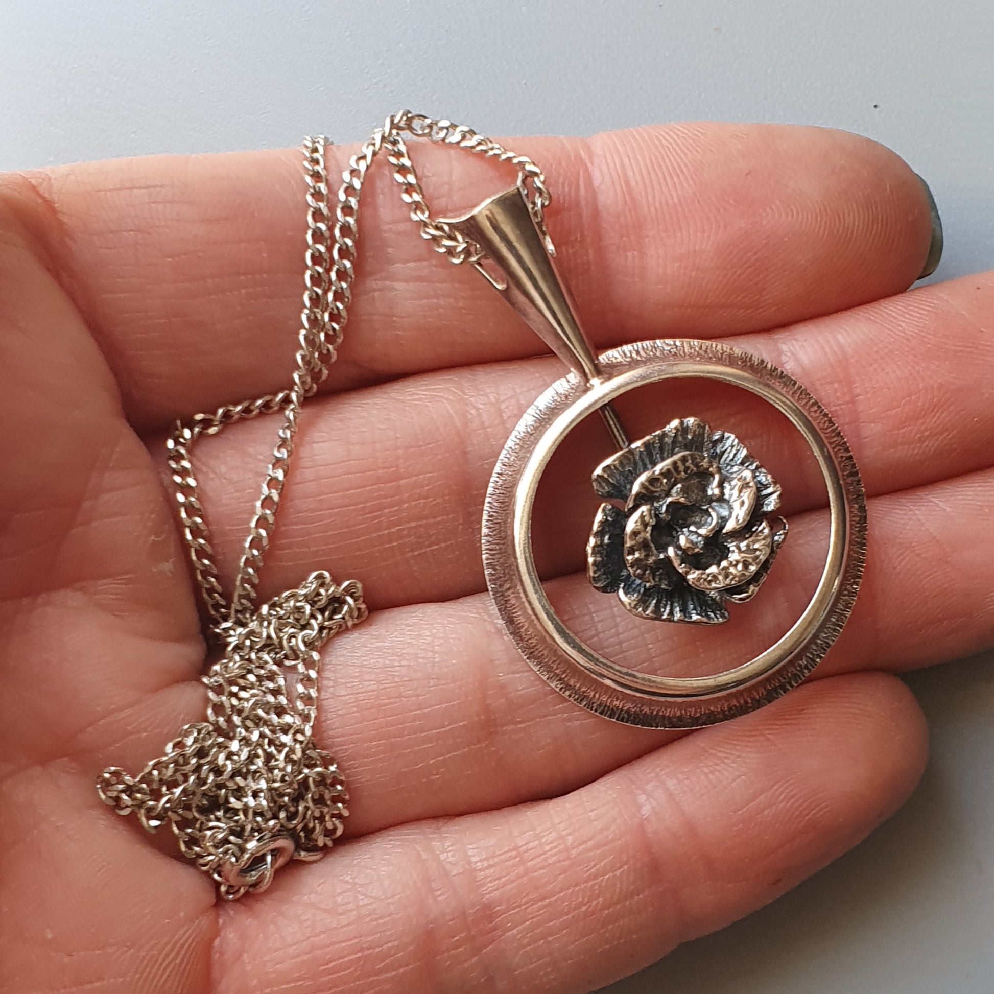 Silver pendant necklace featuring a circular frame with a rose design inside.