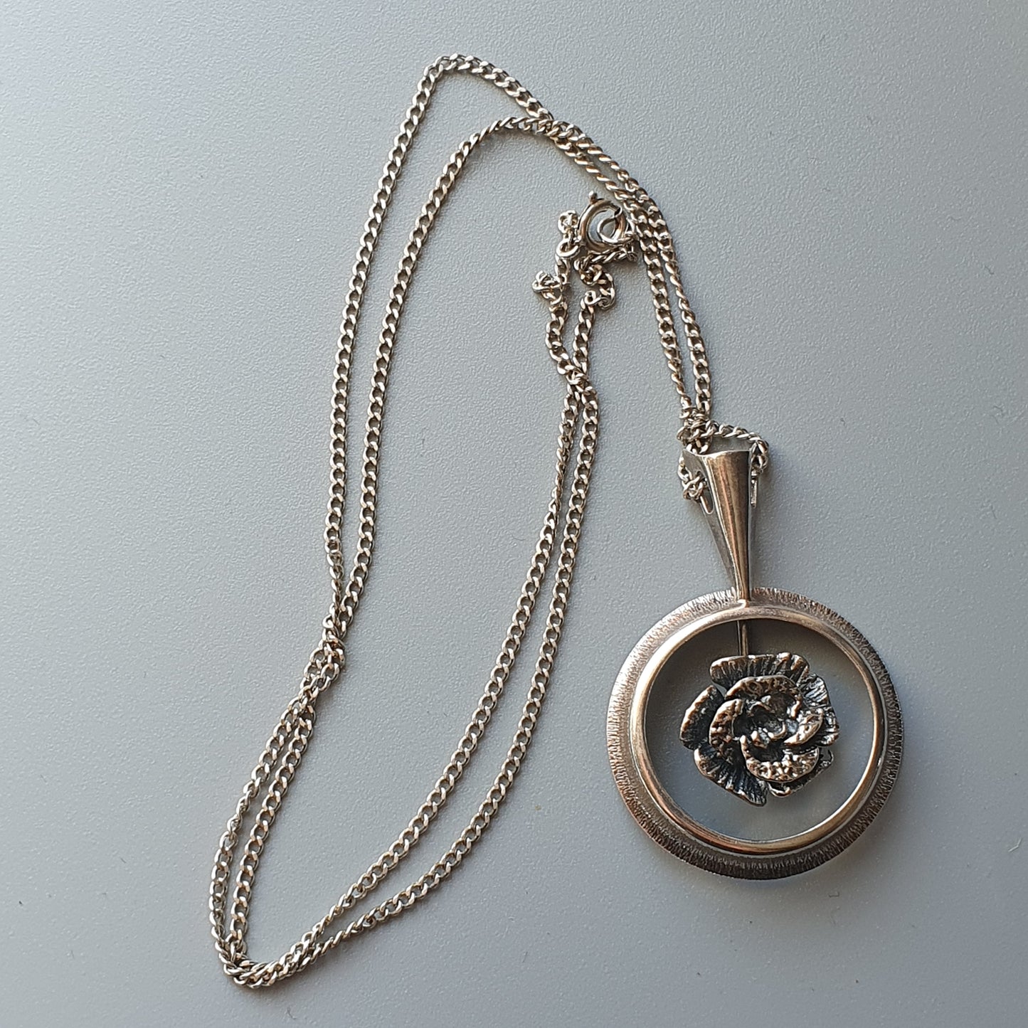 Silver pendant necklace with a circular locket featuring a floral design.