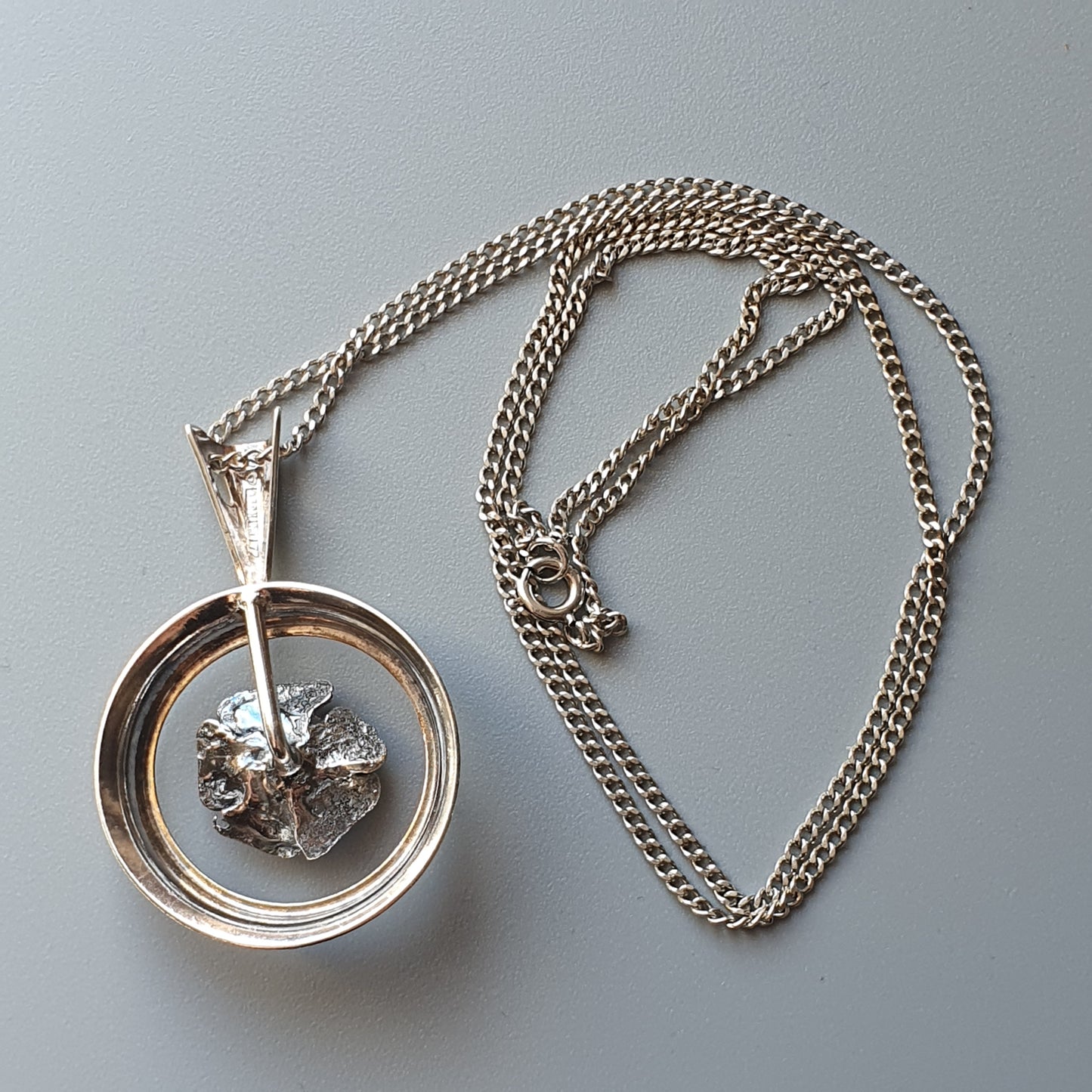 Silver pendant necklace featuring a circular frame with a small meteorite or rock fragment suspended inside.