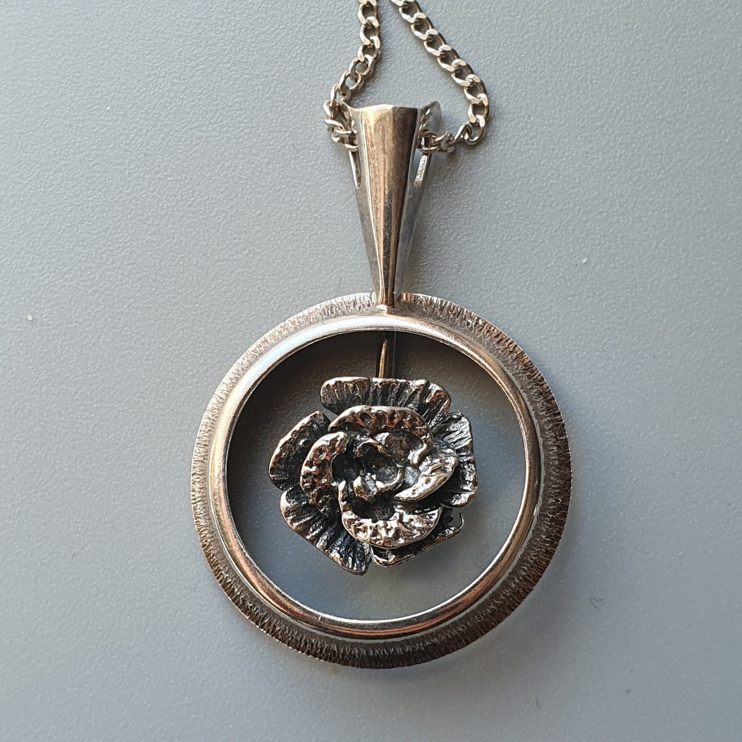 Silver pendant necklace featuring a circular frame with a floral design in the center.