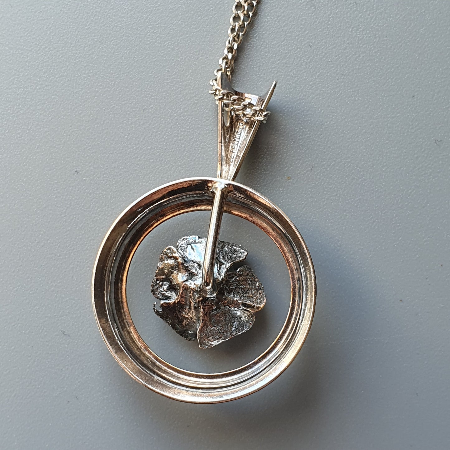 Silver pendant necklace featuring a circular frame with a textured metallic element suspended inside.